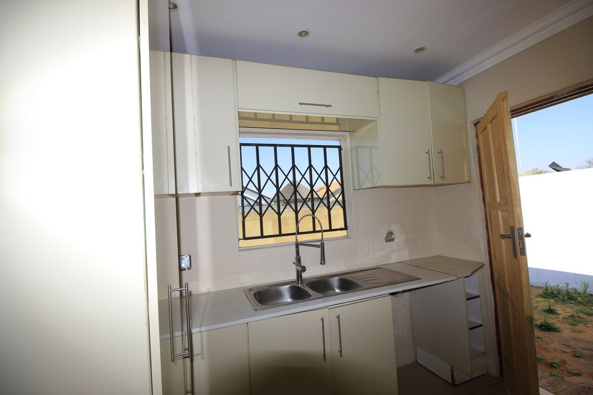 A compact kitchen area featuring built-in cabinetry, a double bowl sink, and direct access to the exterior, currently requiring finishing touches to wall surfaces.
