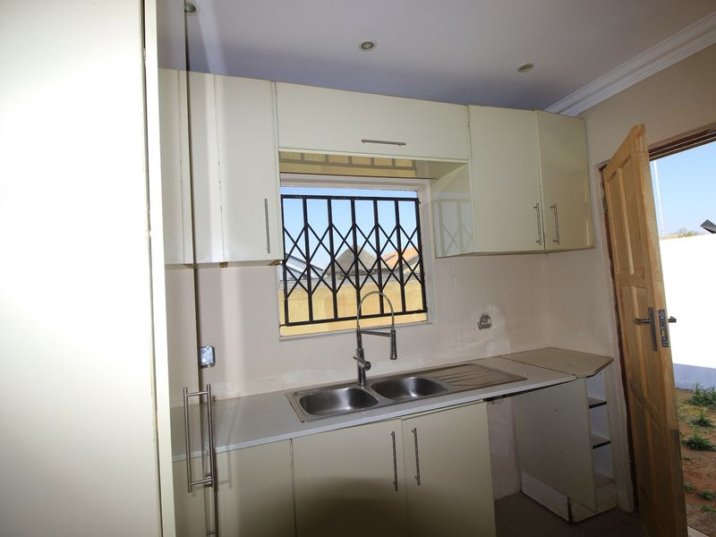 A compact kitchen area featuring built-in cabinetry, a double bowl sink, and direct access to the exterior, currently requiring finishing touches to wall surfaces.