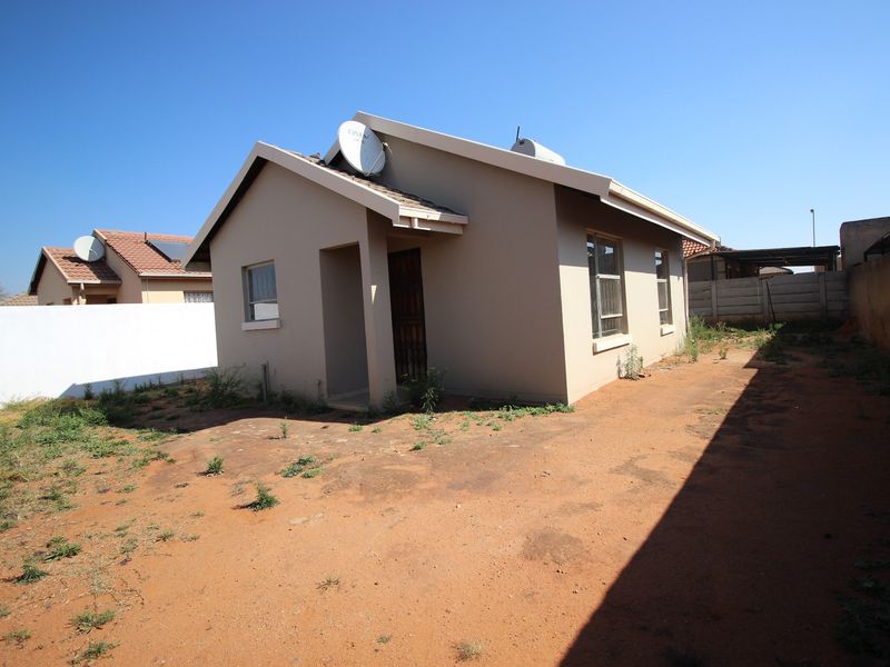 Rear view of a detached house featuring a tiled roof, satellite dish, solar geyser, and a large, unlandscaped yard enclosed by a precast concrete wall.