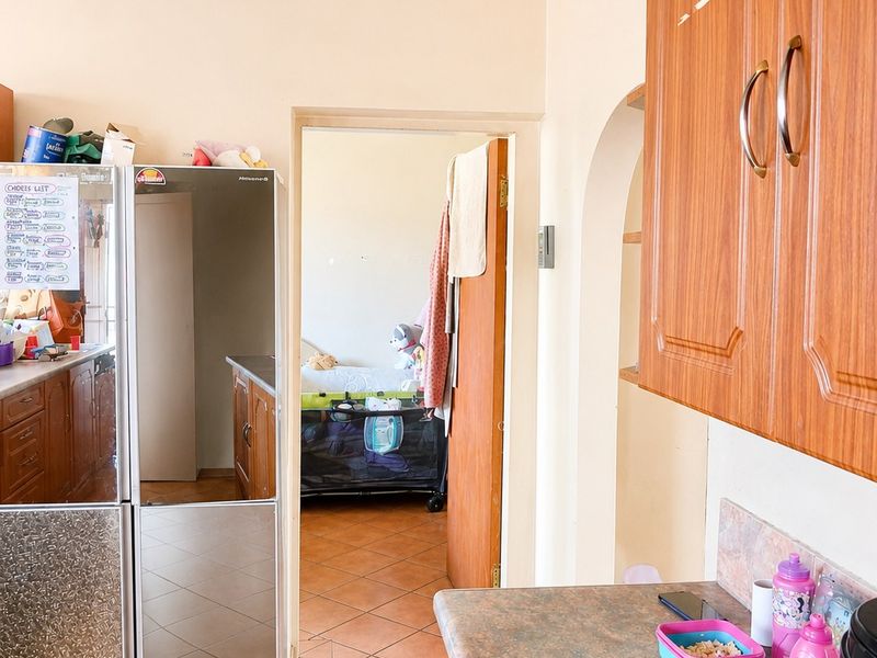 A functional kitchen featuring wooden cabinetry, laminate countertops, and ceramic floor tiles, with an open archway leading to an adjacent room.