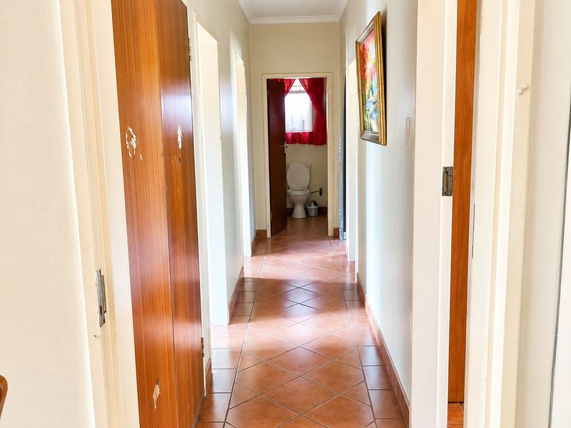 A functional hallway featuring tiled flooring and built-in wooden cupboards, providing access to adjacent rooms including a bathroom.