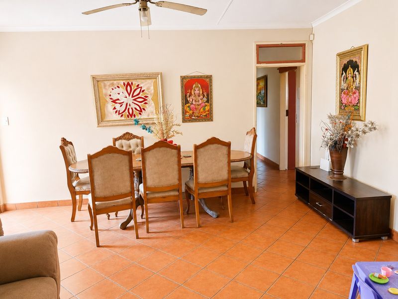 A dining room featuring terracotta floor tiles, a ceiling fan, and a doorway leading to an adjacent hallway.