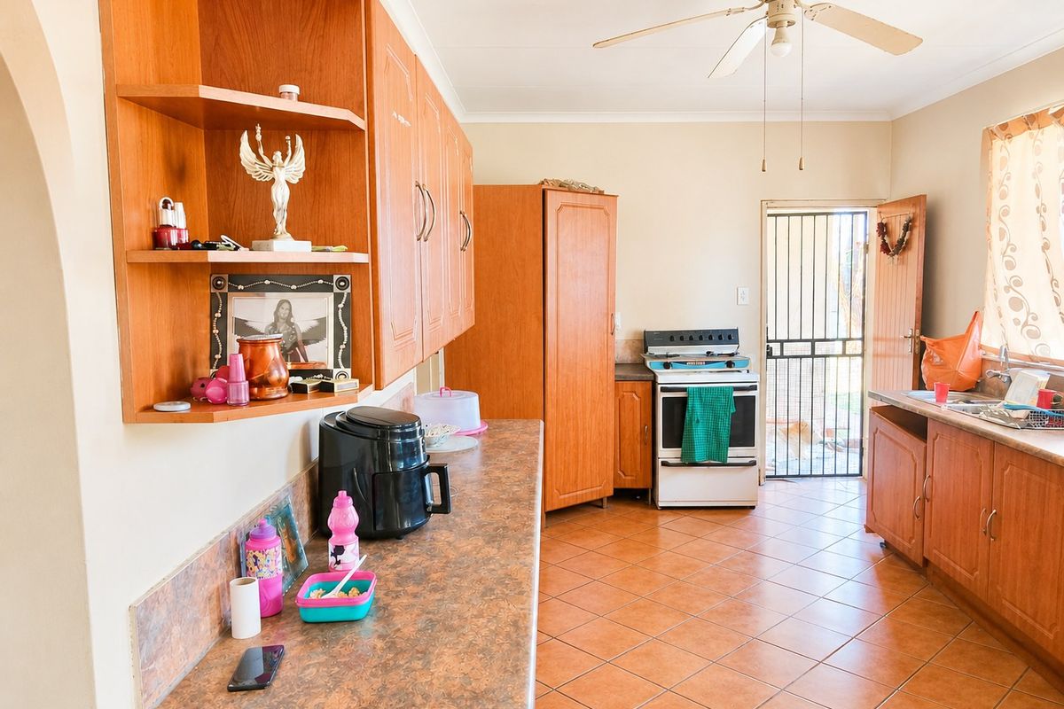 A functional kitchen featuring wood-look cabinetry, laminate countertops, tiled flooring, and a freestanding stove with direct access to the exterior.