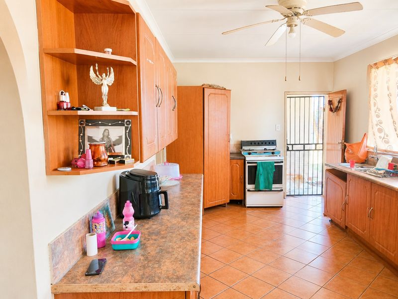 A functional kitchen featuring wood-look cabinetry, laminate countertops, tiled flooring, and a freestanding stove with direct access to the exterior.