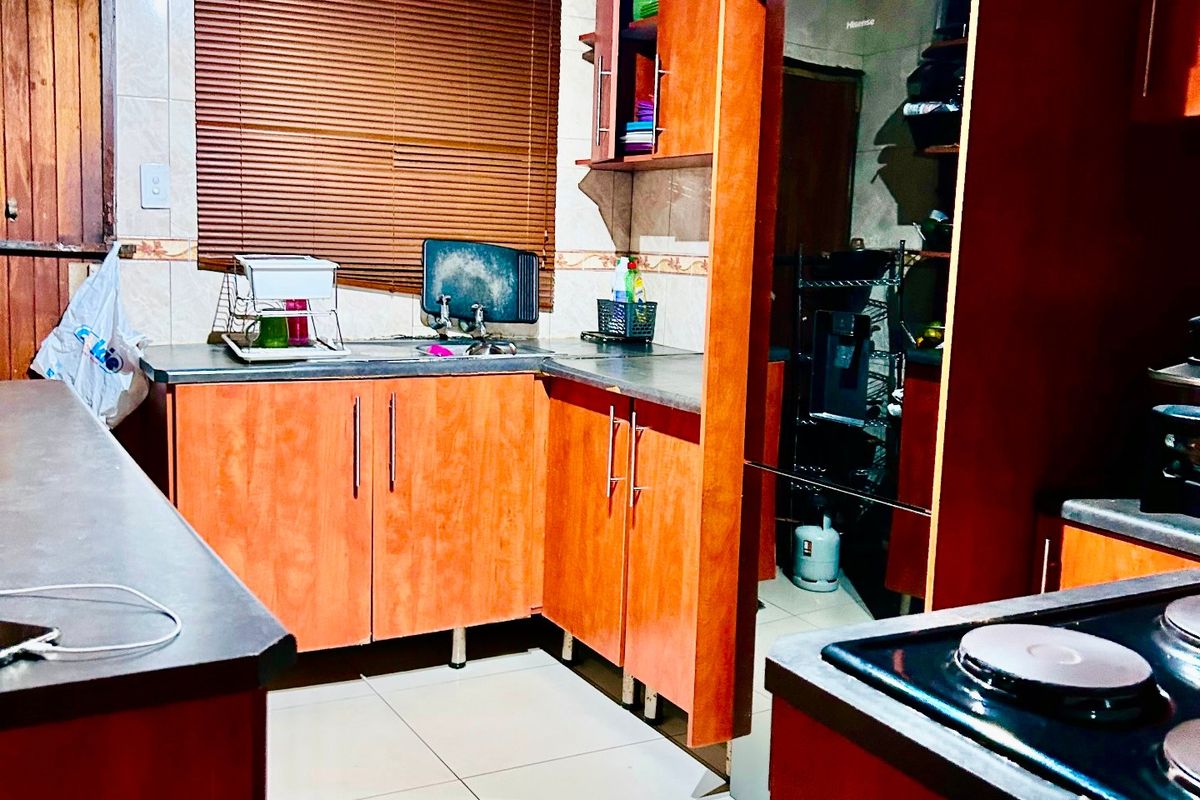 A functional kitchen featuring warm-toned laminate cabinetry, dark countertops, ceramic tiled flooring, and an integrated electric hob with an extractor fan.