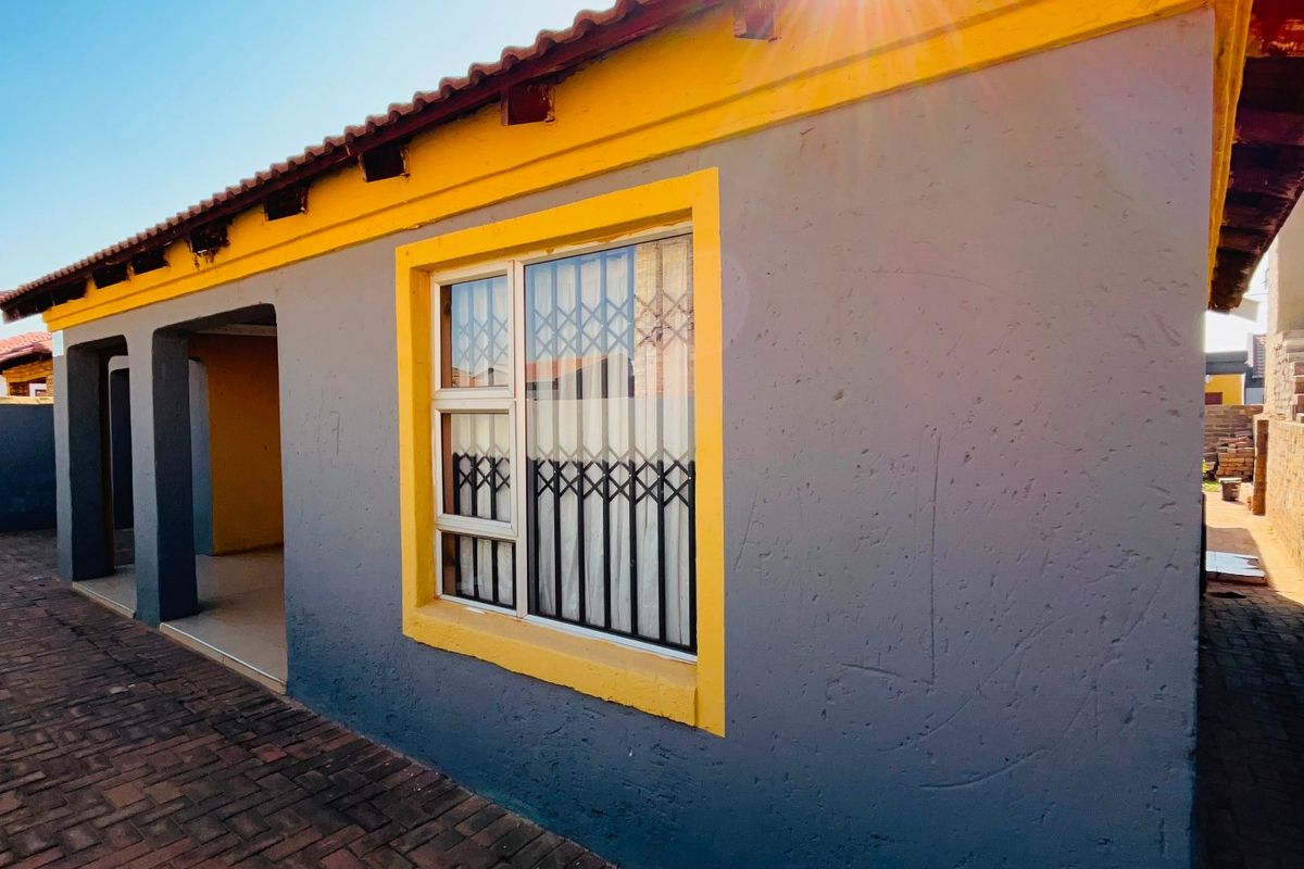 A view of the rear exterior of the house featuring a paved patio area, security gates on windows, and a tiled roof.