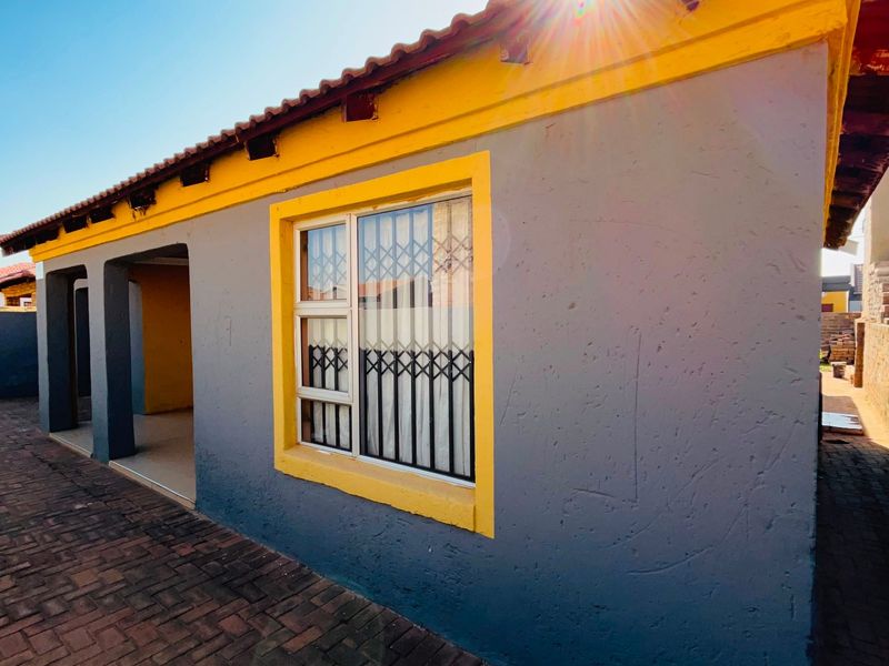A view of the rear exterior of the house featuring a paved patio area, security gates on windows, and a tiled roof.