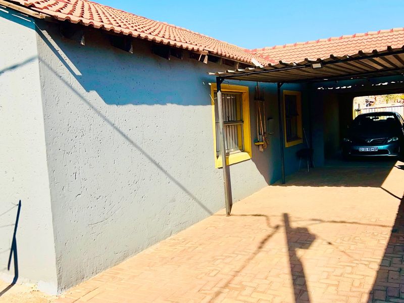 Exterior view of a house featuring a paved driveway, a covered carport area, and a tiled roof with visible maintenance requirements.