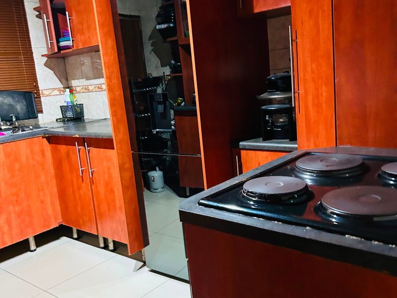 A functional kitchen featuring warm-toned wooden cabinetry, tiled flooring, and a built-in electric hob with ample storage space.