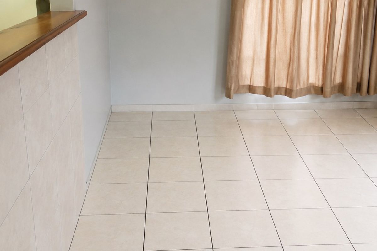 An empty living area featuring neutral tiled flooring and a convenient serving hatch with a timber counter, providing an open feel to the space.