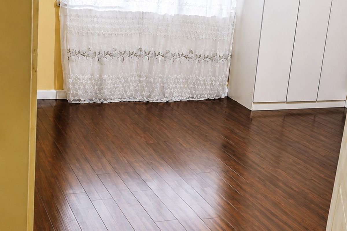A bright bedroom featuring dark laminate flooring, a built-in wardrobe, and a large window with natural light.