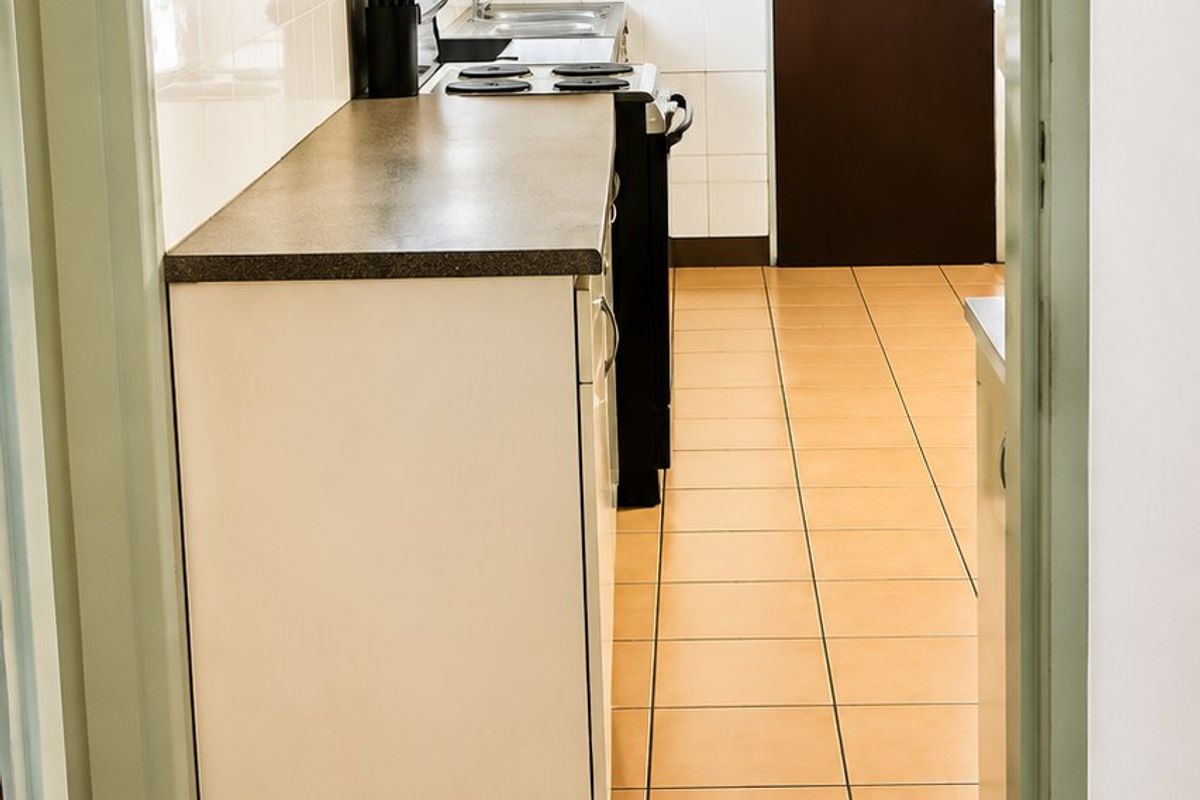 A functional galley-style kitchen featuring tiled flooring, laminate countertops, built-in cabinetry, and a tiled backsplash.