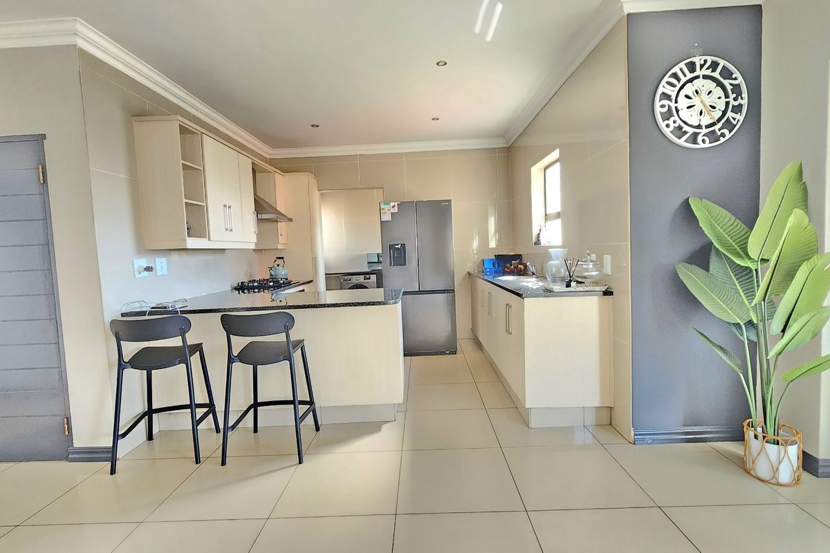 Modern kitchen featuring granite countertops, ample built-in cabinetry, a gas hob with extractor fan, and sleek tiled flooring in an open-plan layout.