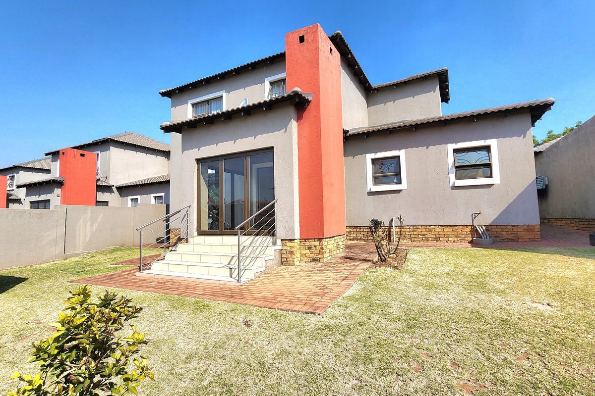 Rear view of the cluster home featuring a paved patio area, stainless steel handrails, and a prominent exterior chimney stack set within a private garden.