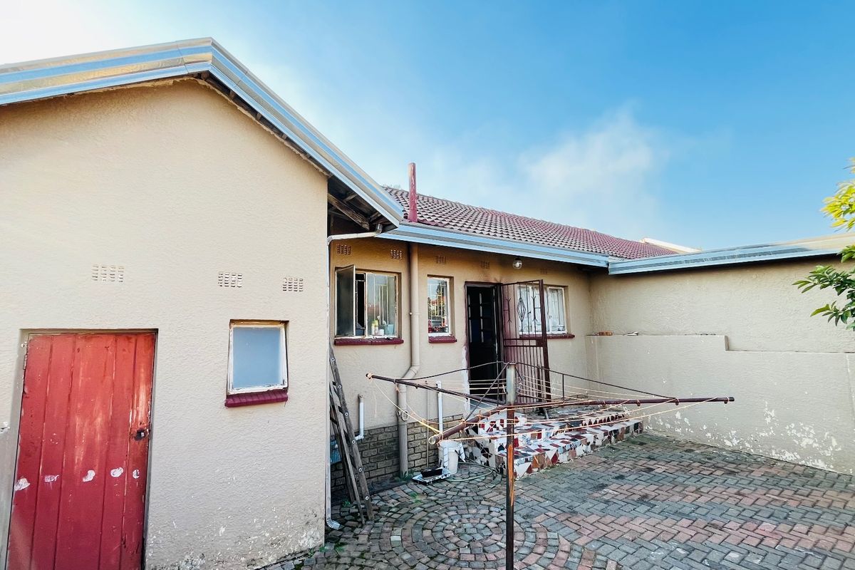 Rear exterior view of the house featuring a paved courtyard, tiled roof, and security gate access.