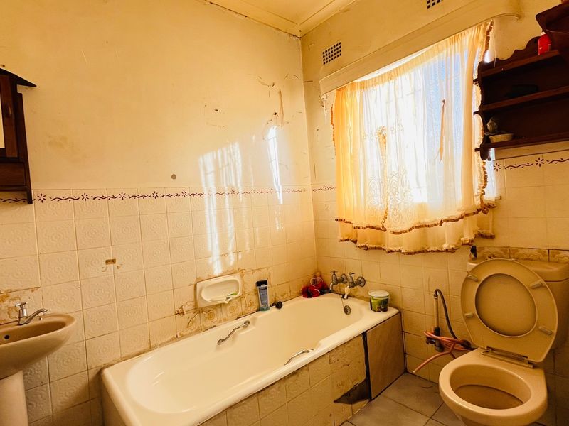 A dated bathroom featuring a pedestal basin, bathtub, and toilet, requiring significant renovation and cosmetic updates to modernize the space.