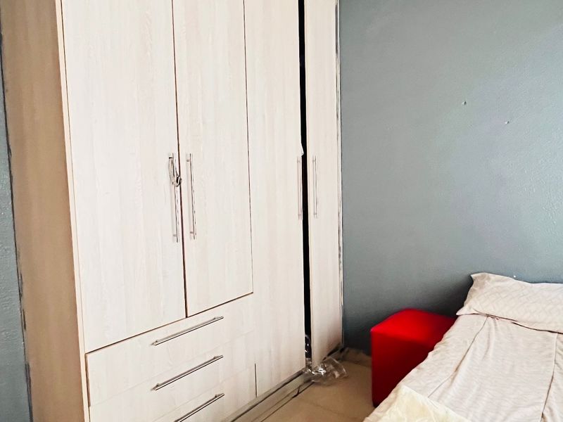 A bedroom featuring a large built-in wardrobe with light wood-grain finish and tiled flooring, requiring minor cosmetic repairs to walls and ceiling.
