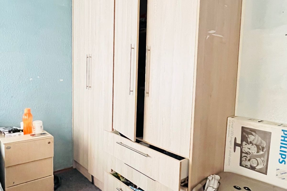 Bedroom featuring a large built-in wardrobe with integrated drawers, requiring cosmetic updates to the walls and flooring to improve overall presentation.