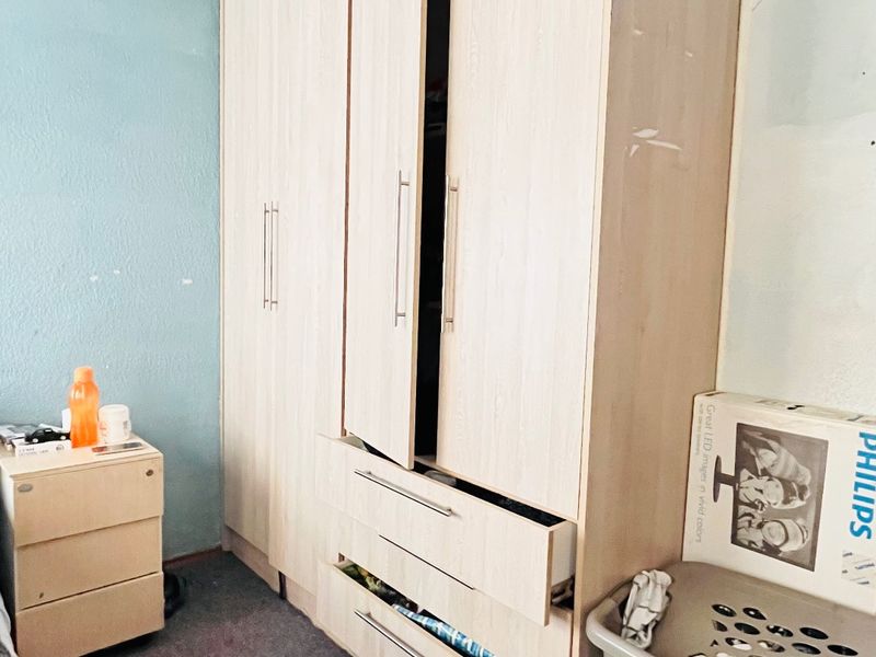 Bedroom featuring a large built-in wardrobe with integrated drawers, requiring cosmetic updates to the walls and flooring to improve overall presentation.