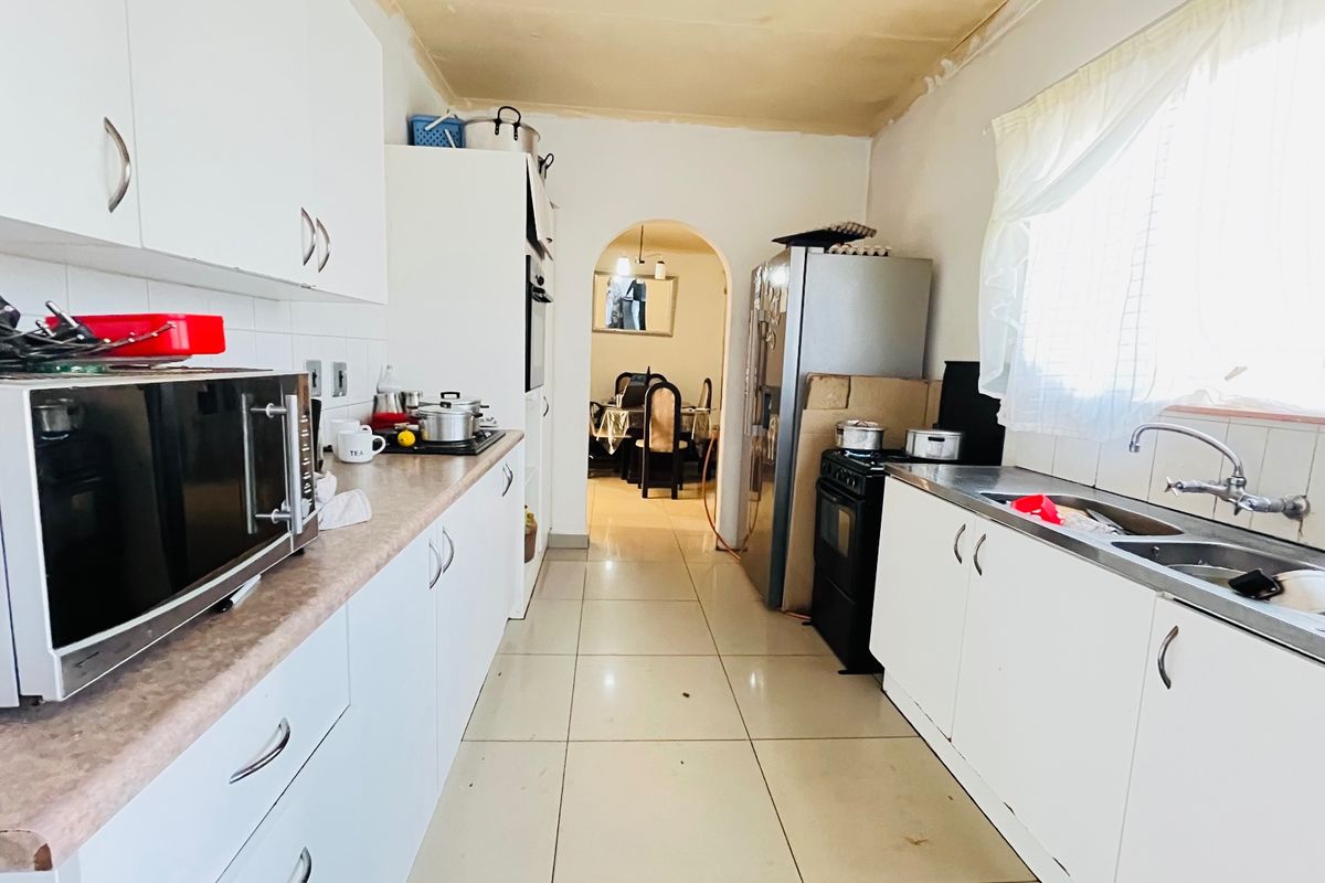 A functional galley-style kitchen featuring white cabinetry, laminate countertops, and a double sink, leading through an archway to the dining area.