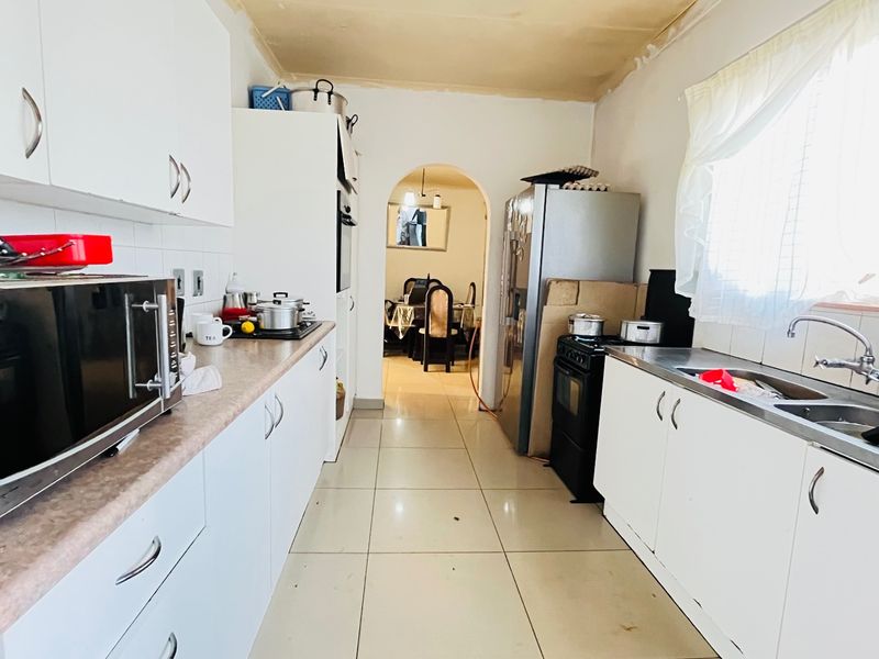 A functional galley-style kitchen featuring white cabinetry, laminate countertops, and a double sink, leading through an archway to the dining area.