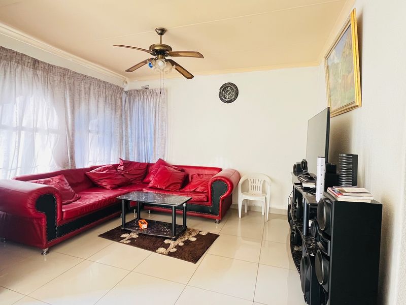A living room featuring tiled flooring, a ceiling fan, and an arched entryway, providing a functional space for relaxation.