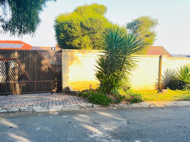 Front view of the property featuring a secure metal driveway gate, perimeter wall, and paved driveway entrance.