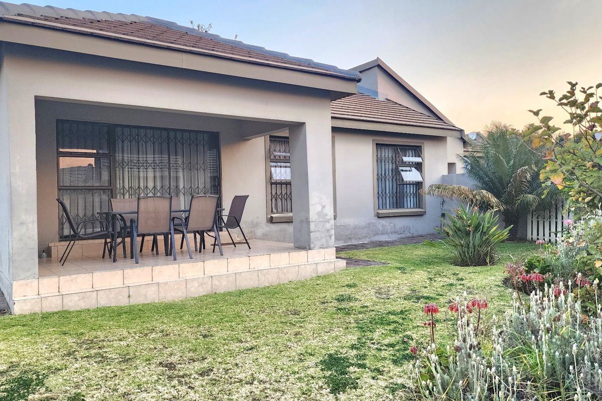 Rear view of the townhouse featuring a covered tiled patio, security gates, and a well-maintained garden area.