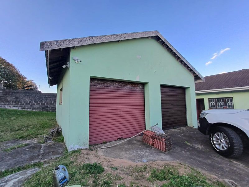 A detached double garage featuring two roller doors, security cameras, and a concrete driveway, showing signs of exterior wear and maintenance requirements.