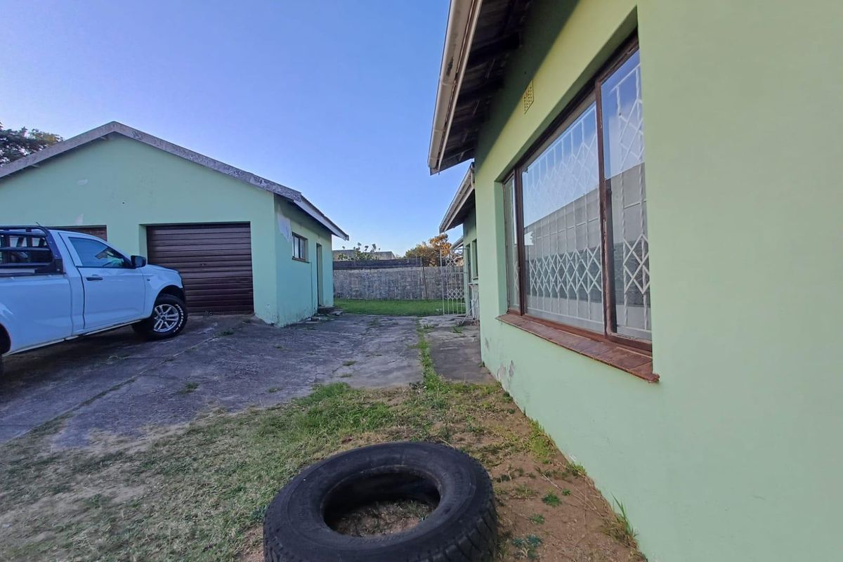 Rear exterior view showing a concrete driveway, detached garage, and the side elevation of the house with security bars on the windows.