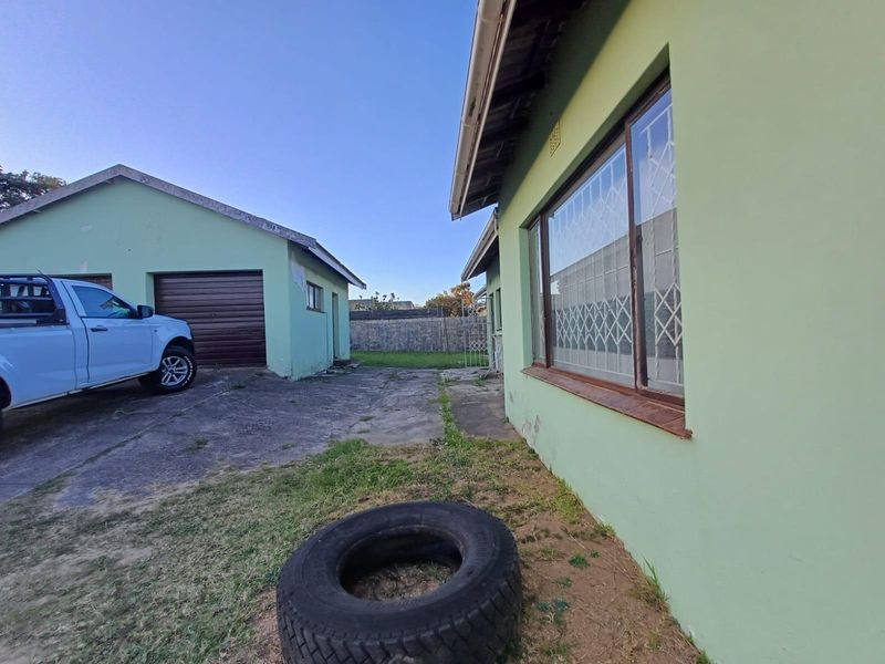 Rear exterior view showing a concrete driveway, detached garage, and the side elevation of the house with security bars on the windows.