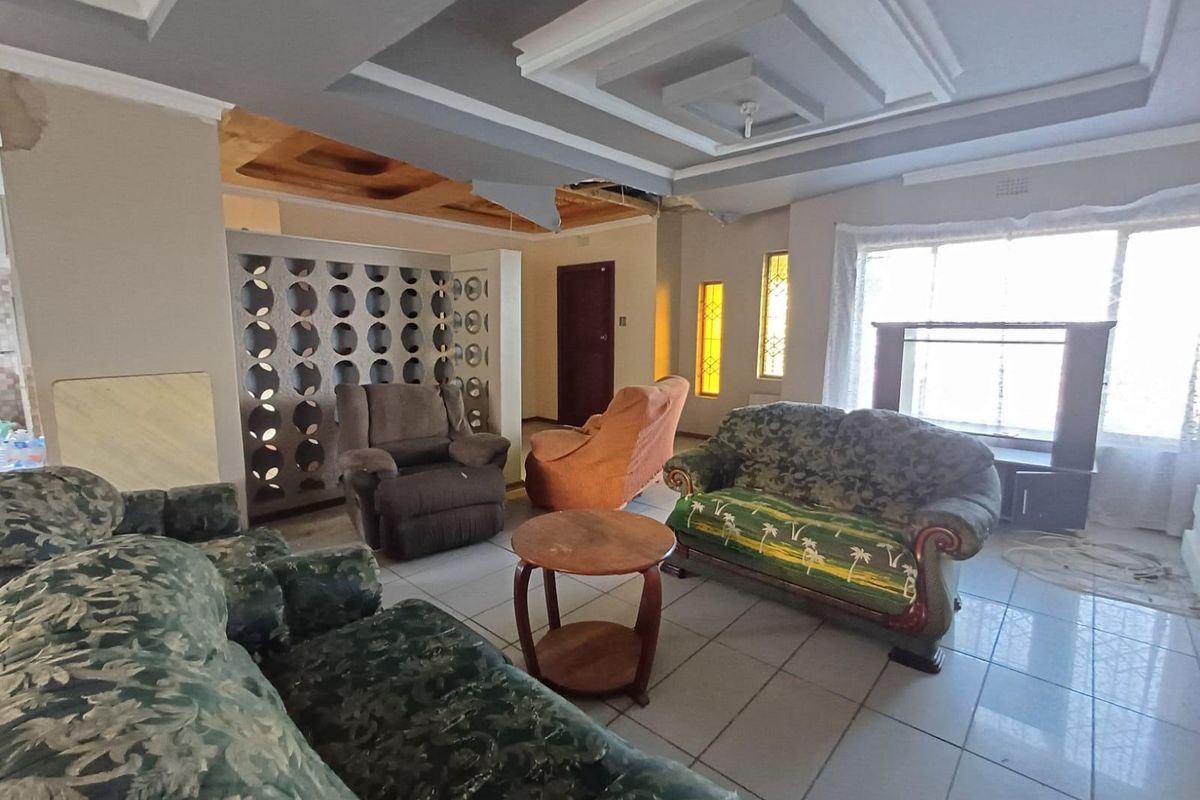 Spacious living room featuring a decorative room divider, tiled flooring, and unique stained glass windows, currently requiring ceiling repairs and cosmetic updates.