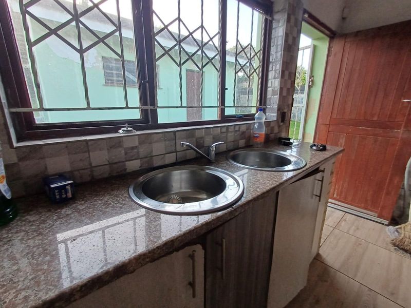 A functional scullery area featuring a double stainless steel sink, granite countertops, tiled splashbacks, and direct access to the exterior.