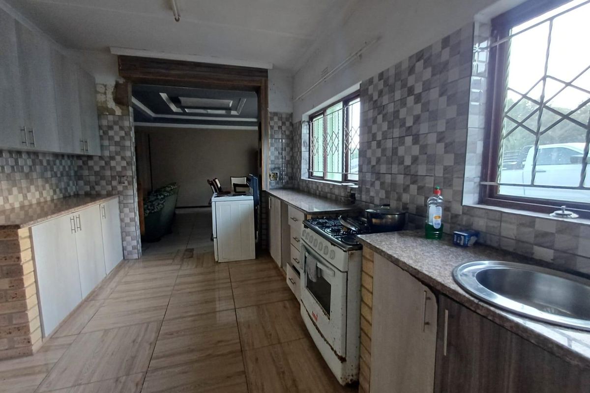 A functional kitchen featuring tiled splashbacks, laminate countertops, built-in cabinetry, and a freestanding stove, with direct access to the adjacent living area.