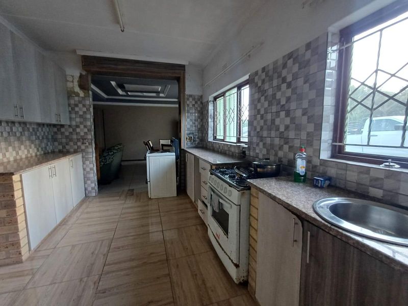 A functional kitchen featuring tiled splashbacks, laminate countertops, built-in cabinetry, and a freestanding stove, with direct access to the adjacent living area.