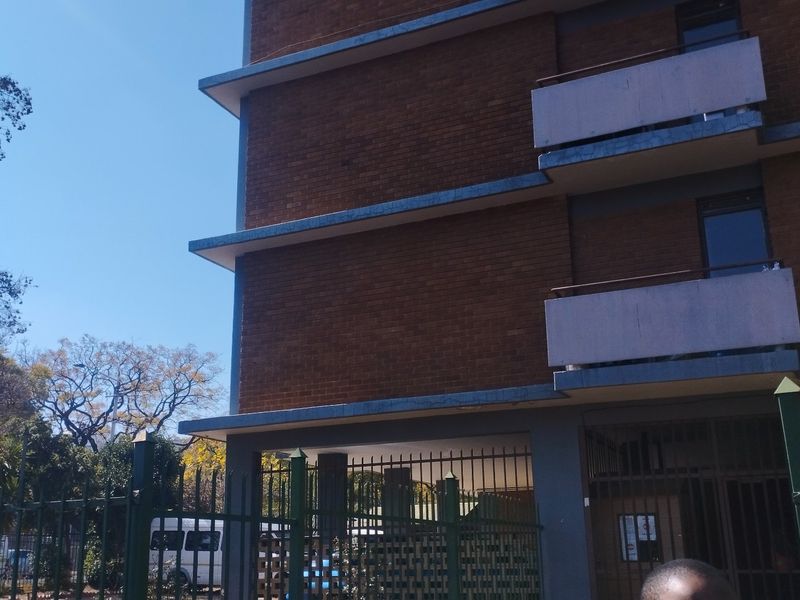 Exterior view of a multi-story brick apartment building featuring private balconies and secure perimeter fencing.