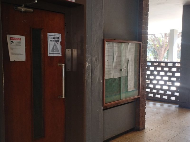 A communal apartment hallway featuring a brick screen wall, tiled flooring, and a notice board, with an elevator currently marked as out of order.