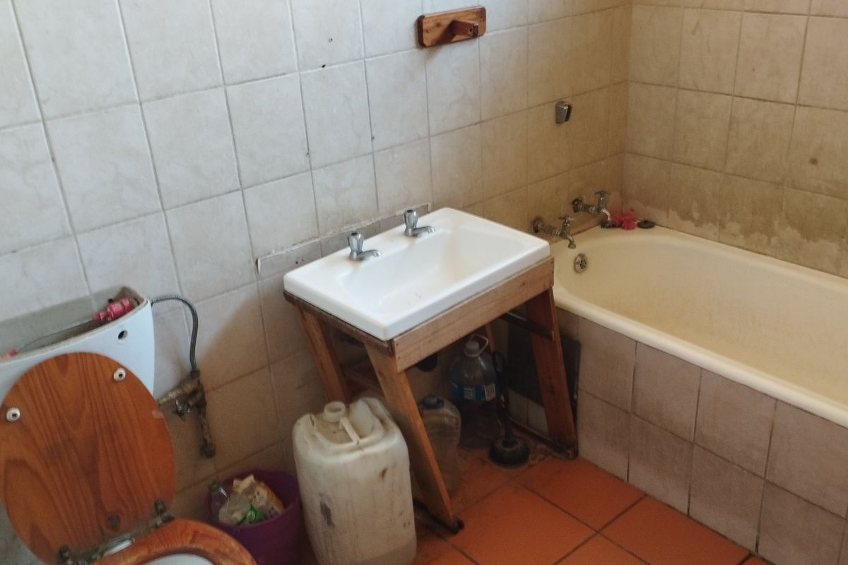 A dated bathroom featuring a standard bathtub, pedestal washbasin, and toilet with tiled walls and flooring, requiring significant renovation and cosmetic updates.