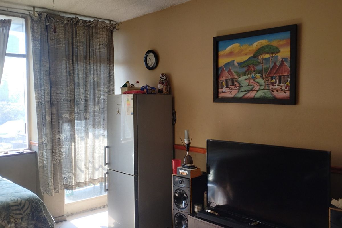 A living area featuring a large window with natural light, chair rail molding, and visible wear on the walls and ceiling.