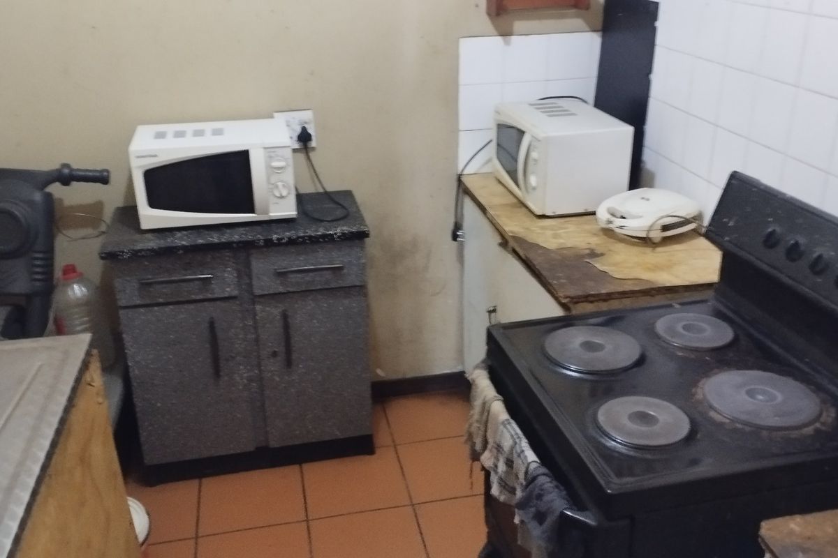A compact kitchen featuring tiled flooring, a tiled splashback, and basic cabinetry. The space requires cosmetic updates and maintenance to improve its overall condition.
