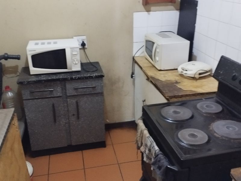 A compact kitchen featuring tiled flooring, a tiled splashback, and basic cabinetry. The space requires cosmetic updates and maintenance to improve its overall condition.