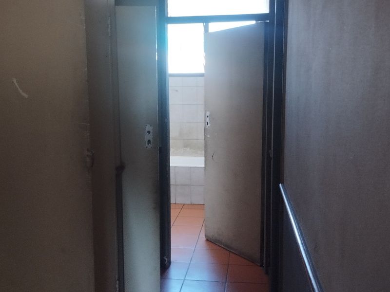 A view through a hallway leading into a bathroom area, featuring tiled flooring and internal doors in need of maintenance.
