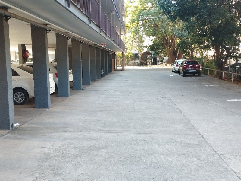 Covered ground-level parking area featuring structural concrete pillars and a paved surface located beneath the apartment building balcony.