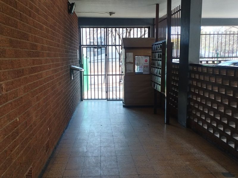 A covered entrance area featuring brick walls, tiled flooring, a security gate, and a row of mailboxes for the apartment complex.