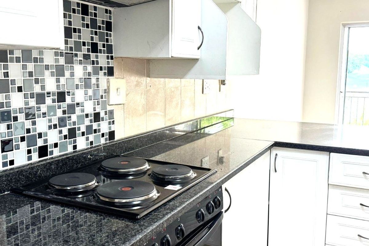 A functional kitchen featuring granite countertops, a built-in oven with electric hob, and a mosaic tile backsplash with white cabinetry.