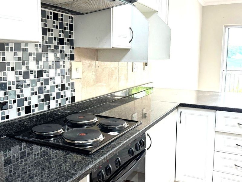 A functional kitchen featuring granite countertops, a built-in oven with electric hob, and a mosaic tile backsplash with white cabinetry.