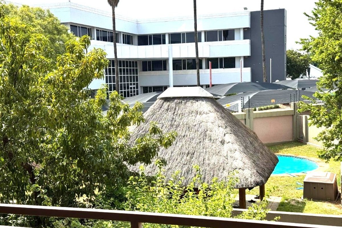 Elevated view overlooking a communal garden area featuring a swimming pool, thatch lapa, and shaded parking facilities within the apartment complex grounds.