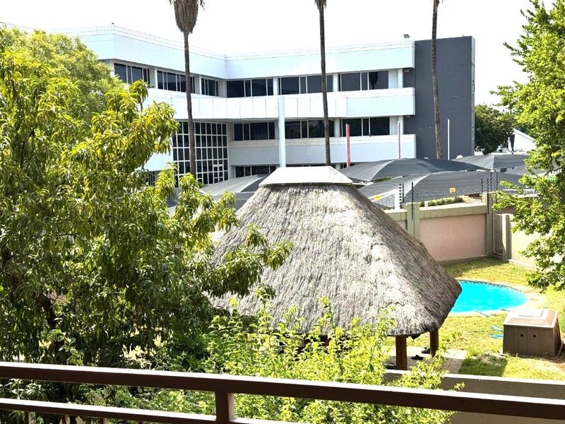 Elevated view overlooking a communal garden area featuring a swimming pool, thatch lapa, and shaded parking facilities within the apartment complex grounds.
