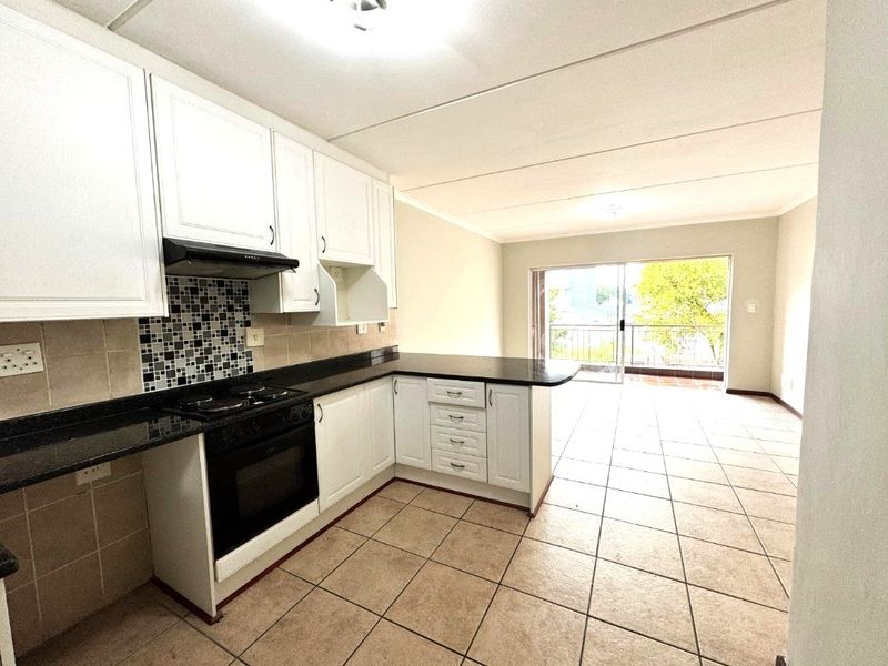 Open-plan kitchen and living area featuring white cabinetry, granite countertops, tiled flooring, and direct access to a balcony through sliding glass doors.
