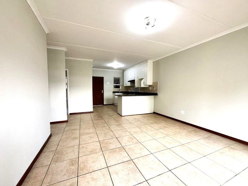 An open-plan living and kitchen area featuring neutral tiled flooring, white cabinetry, and a breakfast counter in a clean, vacant space.